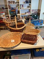 Table display of seven assorted wicker and straw baskets showing various sizes, shapes, and colors with bookshelves and toys in background