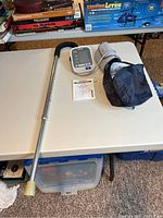 Photo showing Omron blood pressure monitor with cuff, carrying case, adjustable metal cane on a white table.