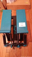 Top angled view of the teal foot pedals with textured grip and the black metal frame with resistance springs visible.
