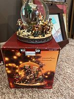 Handpainted porcelain musical globe with carolers figurine scene inside glass dome, shown on top of original Kirkland box.