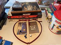 Photo showing stacked boxes of Battleship, Shadowlord, US Traveler games, and open circular wooden Backgammon set with pieces on table