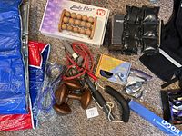 Photo showing assortment of fitness gear: dumbbells, body roller massager, weighted wrist/ankle straps, jump rope, hand exerciser, yoga mat, workout gloves, and boxed door bar.