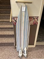Full view of ironing board propped on carpeted stairs with two irons placed at the bottom