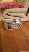 Laundry basket with pink textured blanket and cream fuzzy blanket visible folded on top.