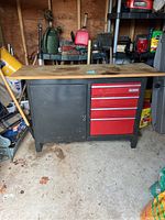 Front view of the Sears Craftsman workbench showing the wooden top, black metal frame, and red drawers with a black cabinet door.