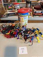 Photo of metal Playskool Tinkertoy container and assorted action figures spread out on table with games in the background