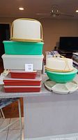 Tupperware lot with cake carriers, storage containers, mixing bowl with base, stacked on kitchen counter.