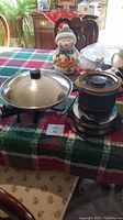 Farberware electric wok with lid, Rival mini slow cooker, and Kenmore waffle iron on a table with a Christmas-themed tablecloth.