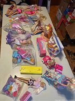 Photo showing a variety of Barbie dolls, accessories, Kelly Power Wheels toy, and other Barbie play items spread on a table.