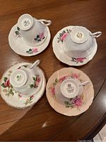 Four tea cups and saucers upside down showing maker's marks: Paragon, Royal Albert, Queen Anne, and another floral pattern. Proves brands and cabbage rose design.