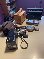Wide view of all items including camera with box, battery, lens hood, weather station, shoe shine box and wine box with tools