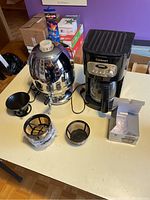 Vintage stainless steel coffee percolator, black Cuisinart coffee maker, coffee filter, coasters on a table
