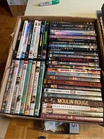 Top-down view of a box filled with DVD movies showing spine titles, identifying various movie titles and confirming the lot contents.