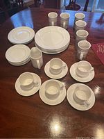 Photo showing the complete lot laid out on a dining table with cups, saucers, creamer, salad plates, dinner plates, dessert plates, and coffee mugs visible.