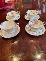 Four tea cups and saucers arranged on wooden table showing different floral patterns and gold trim