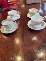 Four tea cups and saucers displayed on wooden table showing overall set composition and design variety