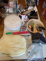 Photo showing Pampered Chef covered baker, various kitchen tools including red and green knife, braided placemat, wooden bowl, and other utensils.