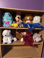 Full view of the plush toy lot arranged on shelves showing 9 various plush toys such as blue Baby Wuv Luv, Minnie Mouse, lion, white polar bear, and others