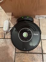 Top-down view of iRobot Roomba on charging dock with power adapter plugged in on tiled floor.