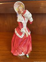 Front view of Royal Doulton Christmas Morn HN3212 figurine showing woman in detailed red dress and bonnet holding a muff.
