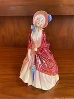 Front view of the Royal Doulton porcelain figure showing a lady in an 18th century style dress with a red paisley shawl and bonnet, holding a parasol.