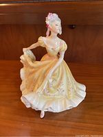 Front view showing detailed yellow dress with pink floral accents, face and hair with floral adornment.