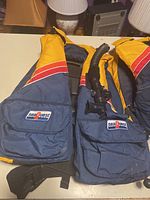 Two Seaquest buoyancy compensators in yellow, navy blue, red, and white with visible inflator and logo patches.