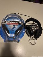 One photo shows a pair of Sennheiser HD 470 headphones inside original sealed retail blue and clear plastic packaging with branding and features visible, next to a loose pair of black Sennheiser headphones.