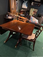 Photo showing the table with folding sides opened partially with two chairs placed around it, displaying the wood finish and design.
