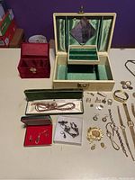 Wide view of assortment of jewelry on table with open cream-colored jewelry box and smaller red box visible