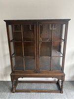 Full front view of oak curio cabinet on woven carpet against white wall