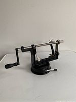 Front side view of the black metal apple corer and peeler showing the suction base and crank handle.