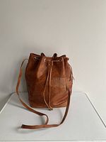 Vintage brown leather bucket bag with hand-stitched details and cinch top closure on white surface