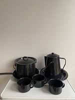 Full set arranged showing lidded pot, kettle, frying pan, three mugs, and deep plates underneath kettle