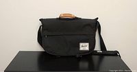 Front view of black Herschel laptop bag with flap top, leather handle detail and adjustable strap.