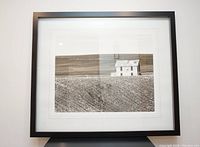 Framed black and white print showing a rural scene with a field and barn, mounted on a wall against a white background.
