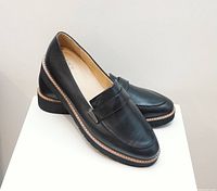 Pair of black leather women's loafers displayed on white pedestal, side and angled views.