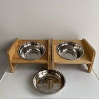 Front view of the two bamboo raised feeding stations each with a stainless steel bowl, plus one separate shallow stainless steel bowl on white surface.