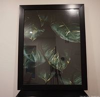 Framed photographic art print depicting large green plant leaves on a dark background.