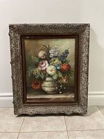 Full view of vintage floral oil painting in large ornate frame against a white wall.