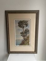 Full view of framed vertical watercolour painting showing coastal landscape with pine trees and sea.