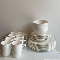 Photo showing 8 stacked dinner plates, 8 stacked salad plates, 7 stacked bowls, and 8 white mugs arranged in front.