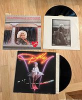 Photo of two Dolly Parton vinyl records: Heartbreak Express and self-titled album with covers and sleeves visible on wooden surface.