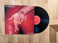 Photo of Loverboy Get Lucky vinyl record partially out of its cover on wooden floor.