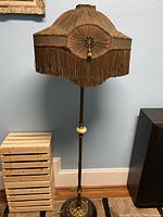 Full view of floor lamp showing scalloped peach fabric shade with fringe and brass-toned metal shaft with onyx accent