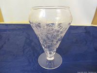 Full view of the clear, hand etched glass vase showing overall shape and design against a blue fabric background.