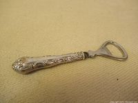 Full view of the Birks sterling silver bottle opener on fabric background showing entire item including patterned handle and metal opener.