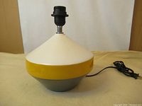 Full view of the ceramic table lamp base with yellow, white, and gray color bands, electrical socket fixture, and cord.