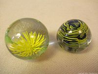 Two vintage glass paperweights; one with yellow flower motif and other with green/black swirl pattern