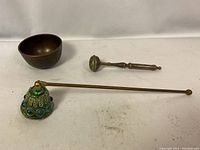 Three metal items on white cloth: heavy copper cup, decorative candle snuffer, small brass/bronze object
